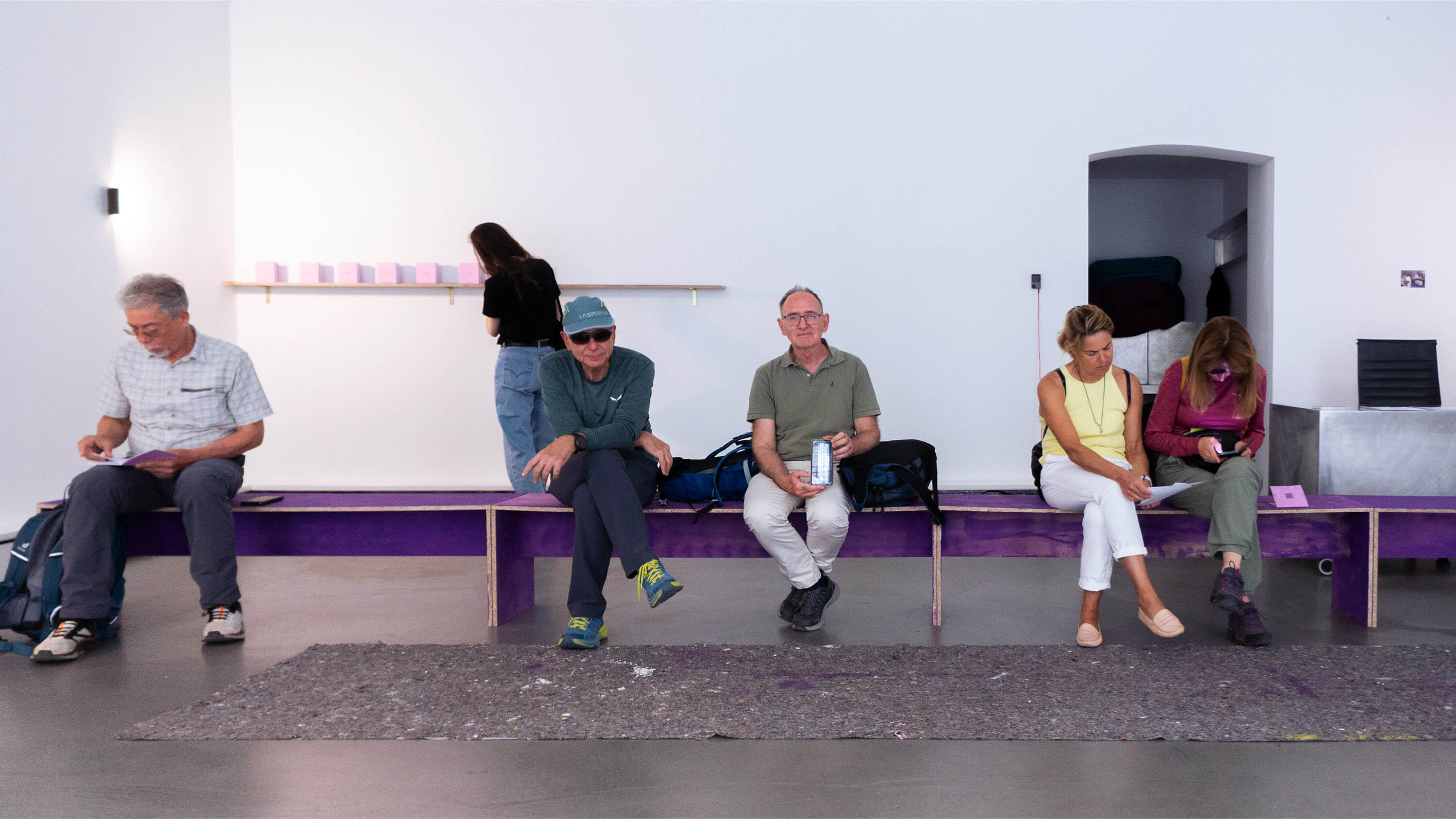 Contemporary art exhibition with speakers, purple benches and people hanging out.